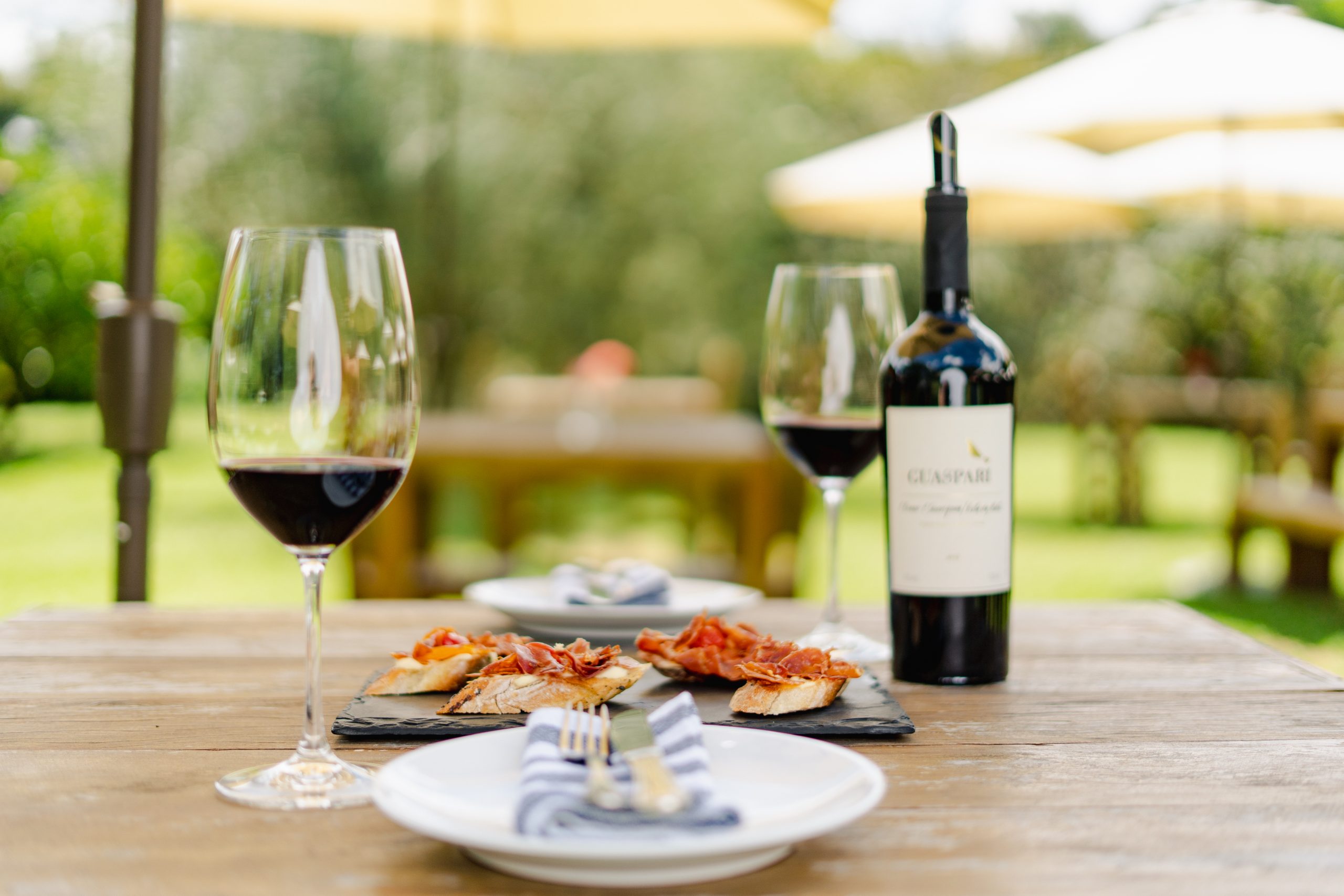 Taça e garrafa de vinho acompanhando aperitivos em uma mesa, representando a combinação de gastronomia e vinhos.